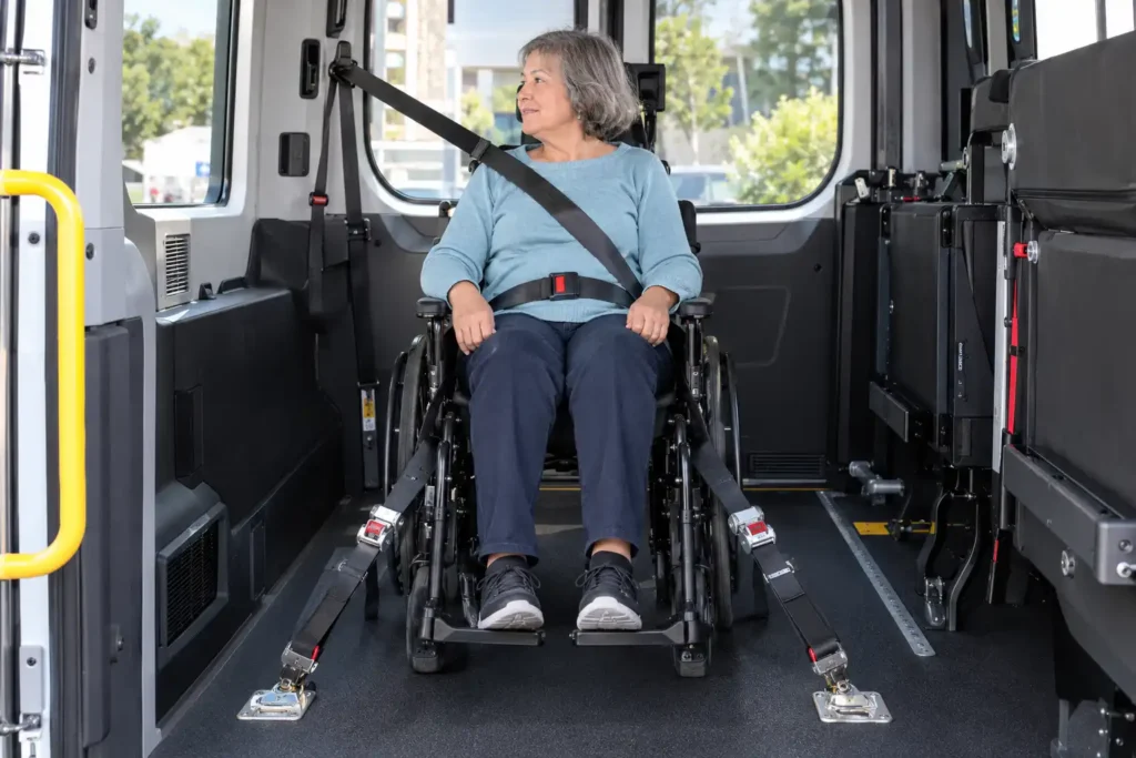 Inside a wheelchair-accessible van showing the securement area and driver assisting a rider